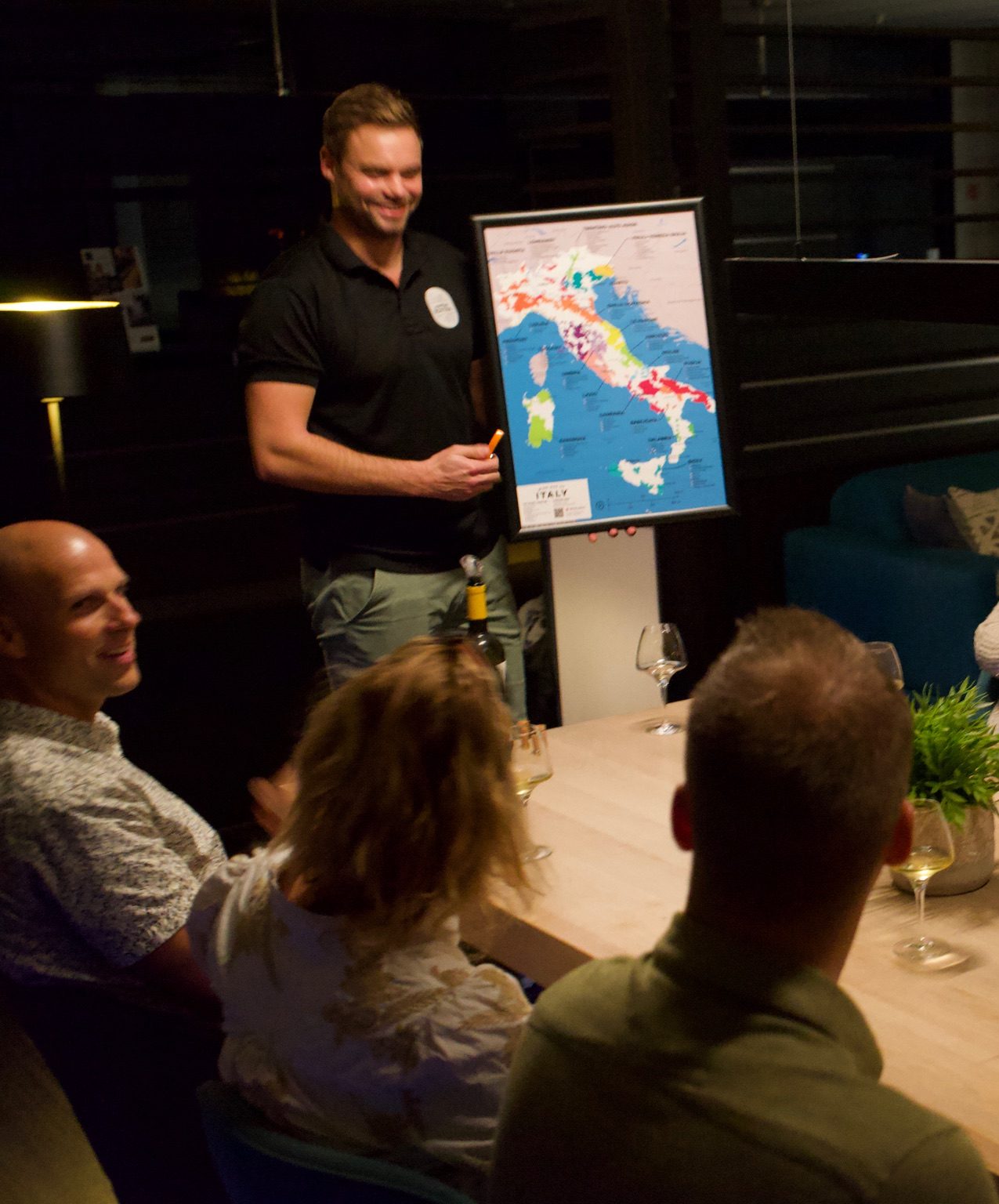 Wijnproeverij aan huis met een sommelier die Italiaanse wijnen presenteert aan een groep mensen aan tafel.