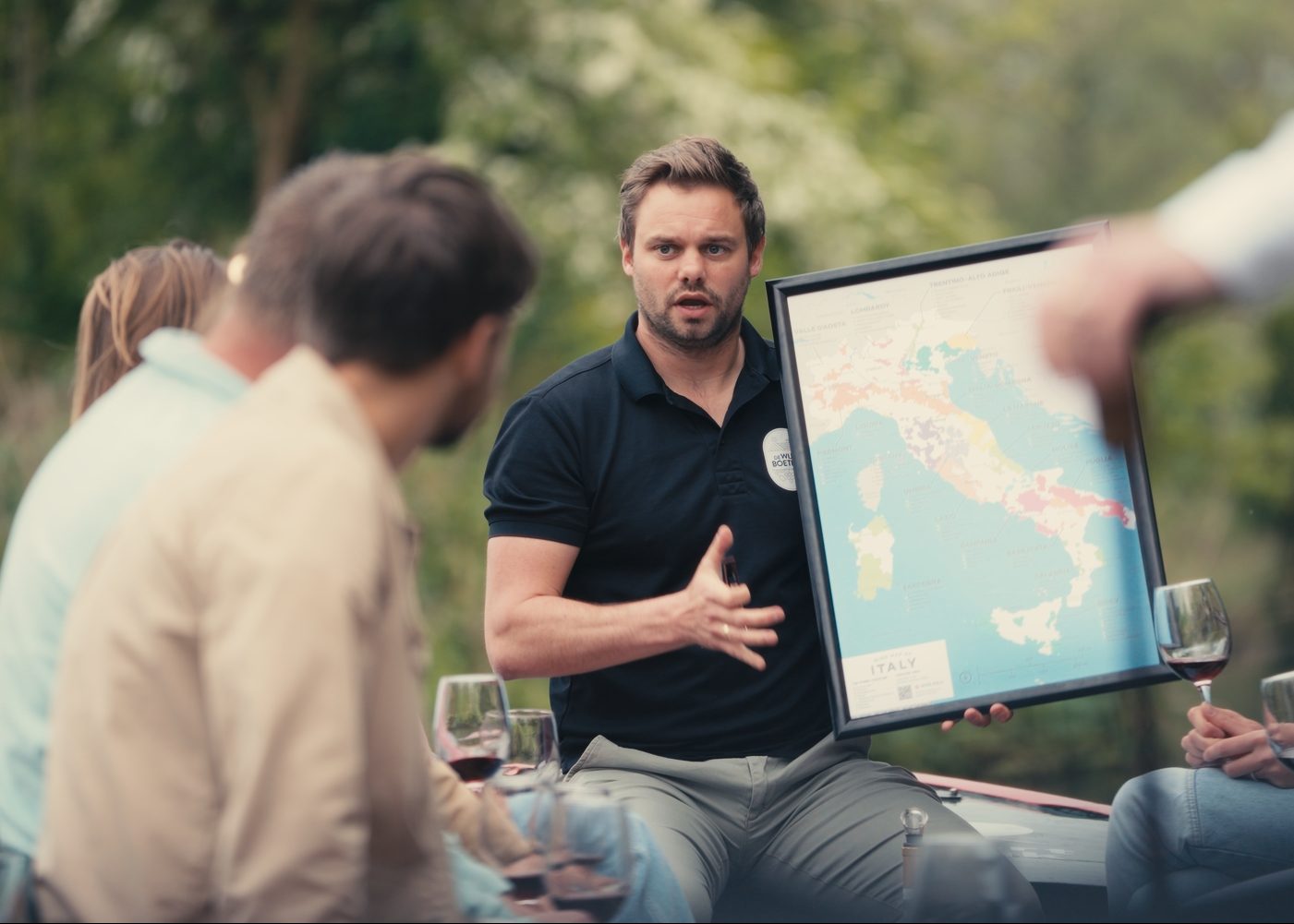 Dennis, eigenaar van De Wijnboetiek, vertelt vol passie over Italiaanse wijn aan een groep geïnteresseerden in een buitenomgeving tijdens de Wijnvaart.
